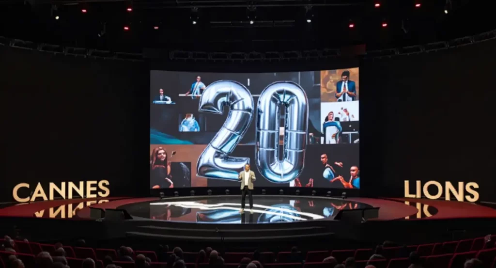 Scène de présentation au festival Cannes Lions avec le chiffre "20" en ballons et des images de participants en arrière-plan.