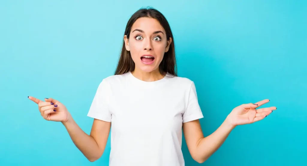 Femme surprise avec les mains levées, exprimant une humeur joyeuse sur fond bleu.