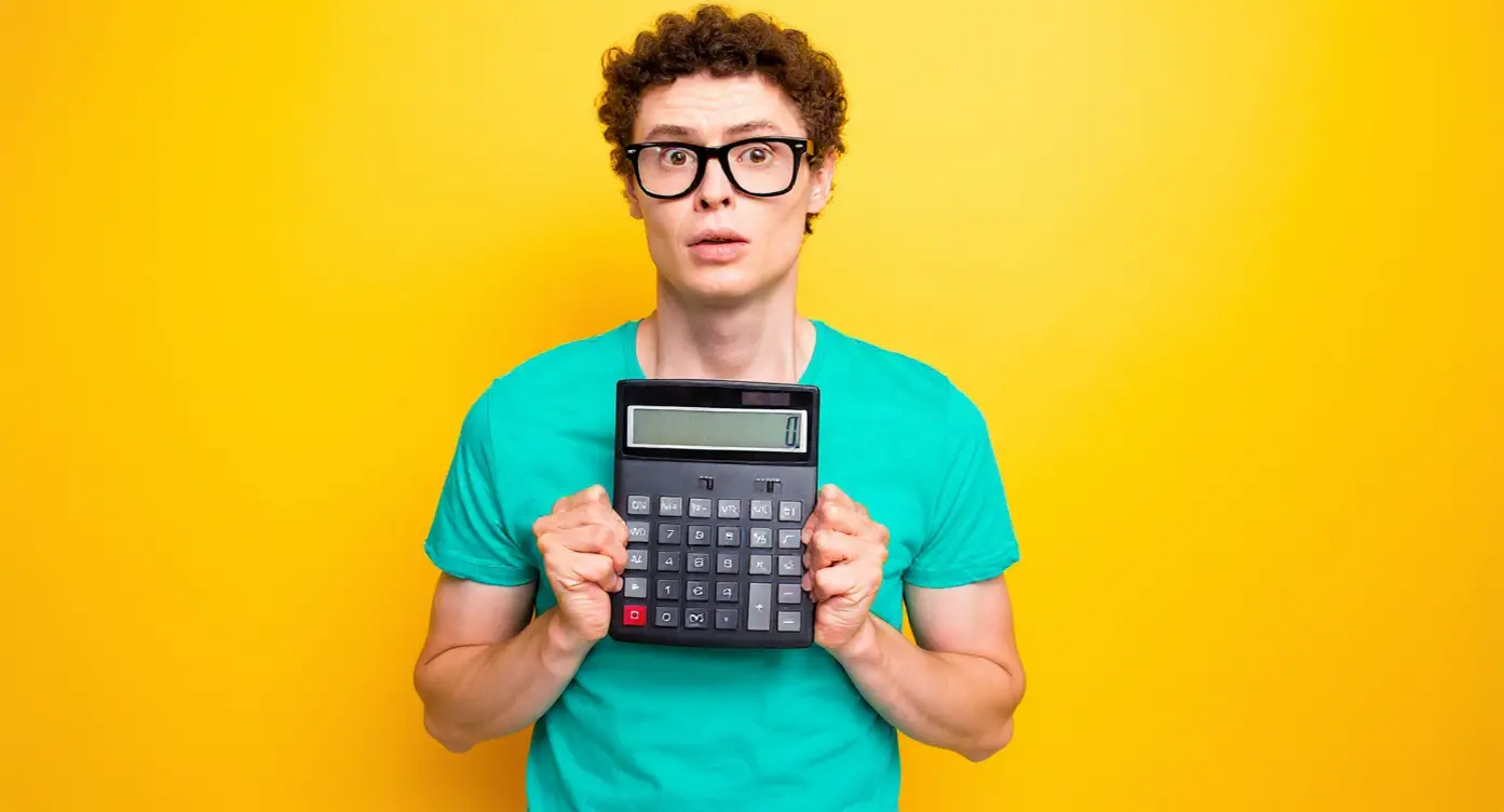 Homme avec lunettes tenant une calculatrice sur fond jaune, affichant une expression préoccupée.