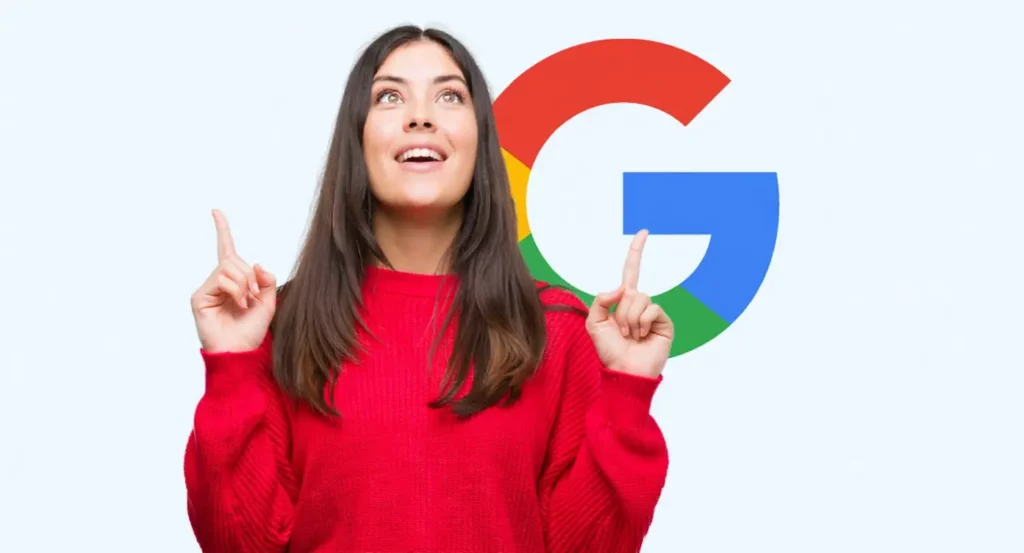 Jeune femme souriante en pull rouge, pointant vers le logo coloré de Google en arrière-plan.