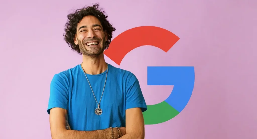 Homme souriant en t-shirt bleu devant un logo Google coloré sur fond rose, illustrant l'innovation technologique.