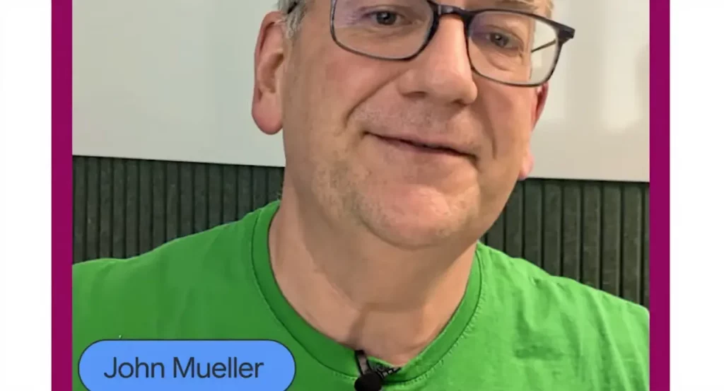 Homme portant des lunettes et un t-shirt vert, souriant, se tenant devant un fond sombre.