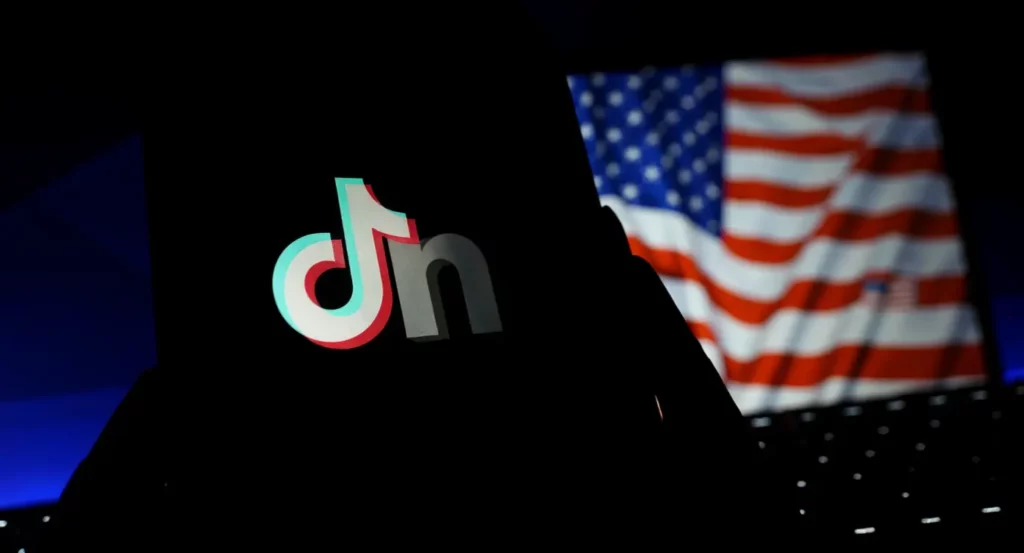 Logo de TikTok en silhouette avec un drapeau américain en arrière-plan flou, symbolisant la culture numérique et les réseaux sociaux.