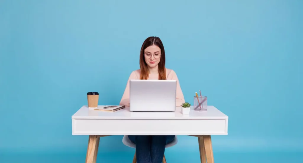 Femme travaillant sur un ordinateur portable à un bureau moderne avec une tasse de café et des fournitures de bureau.