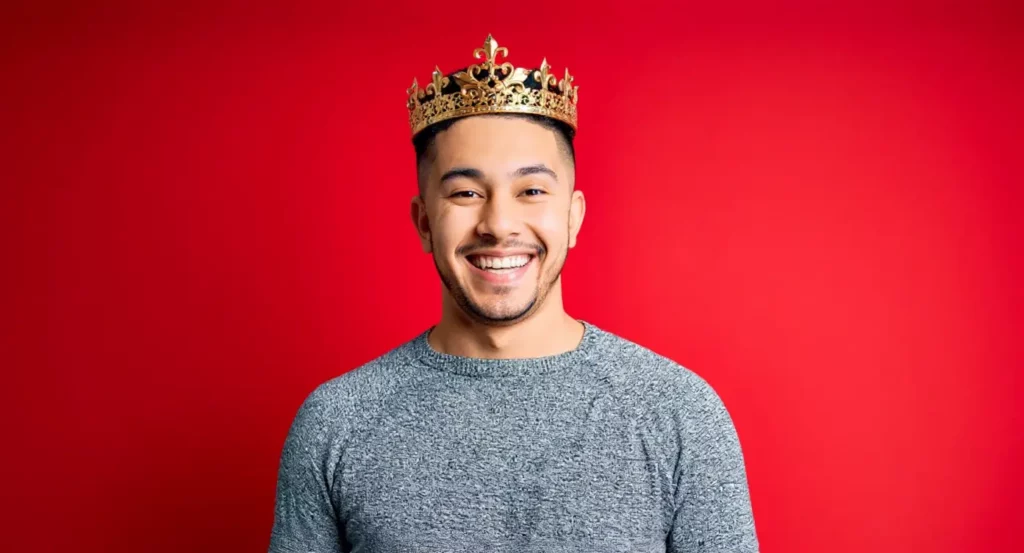 Homme souriant portant une couronne dorée, devant un fond rouge vibrant.