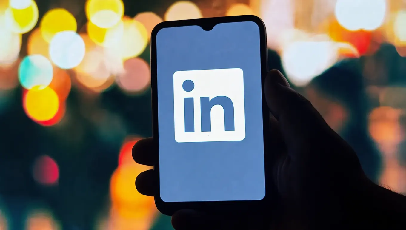 Écran de smartphone affichant le logo LinkedIn, avec un fond flou de lumières colorées.