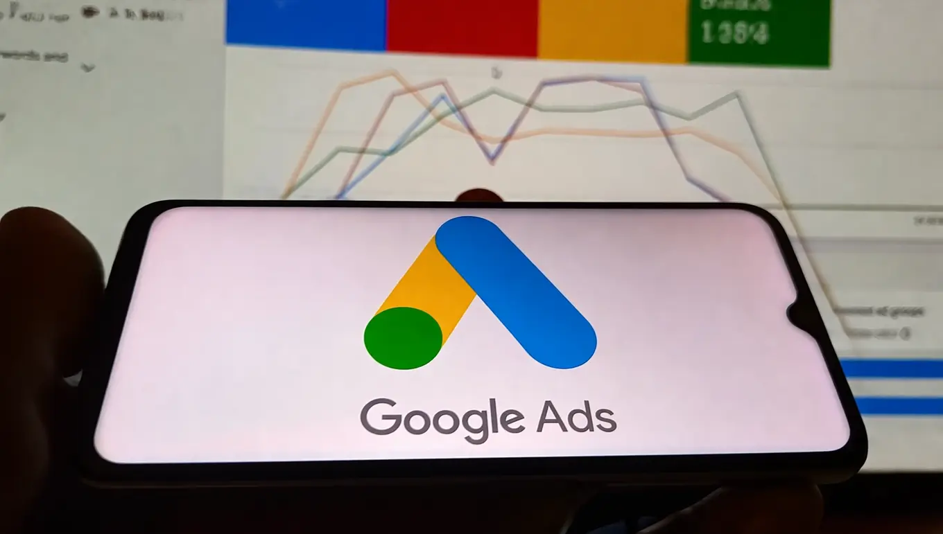 Logo de Google Ads affiché sur un smartphone avec des graphiques analytiques en arrière-plan.