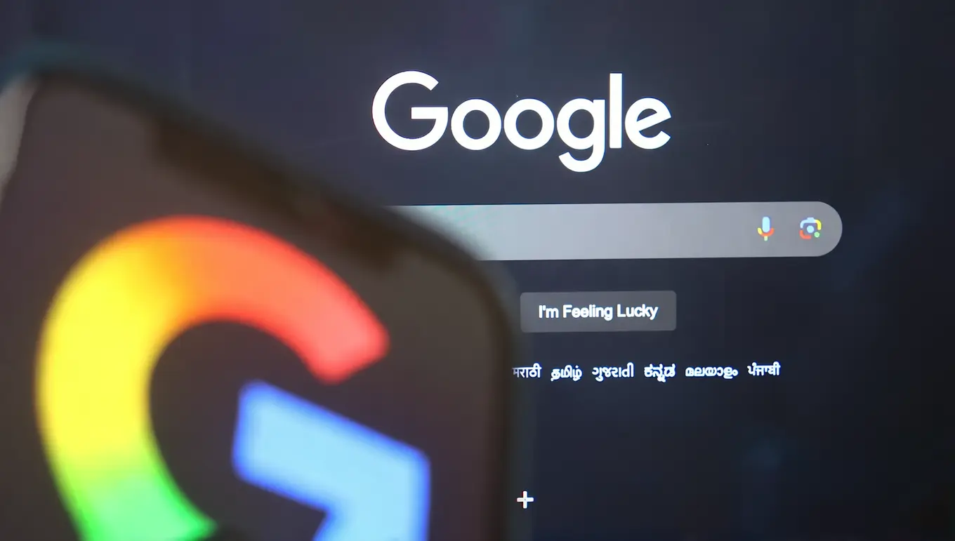 Logo coloré de Google en premier plan avec la page d'accueil de Google en arrière-plan sur un écran.